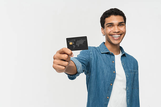 istock Young Man Smiling and Presenting Credit Card Against White Background 2205895675