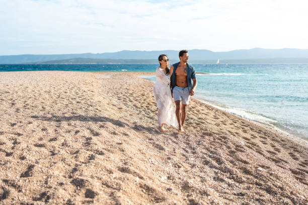 istock Romantic Mid-Adult Couple Walking Along Sun-Drenched Mediterranean Beach Shore 2205896049