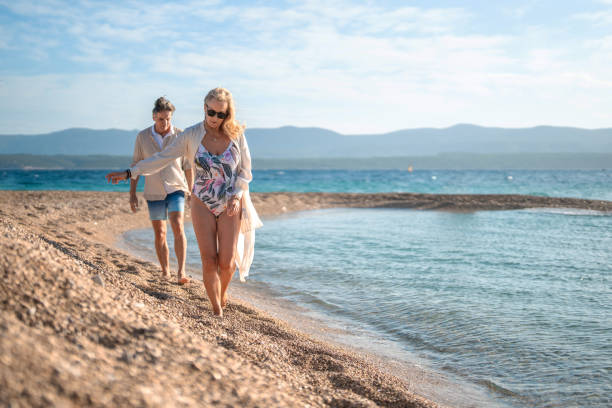 istock Relaxed Caucasian Mature Couple Strolling Along Sunny Pebble Beach 2205896099