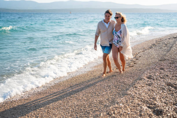 istock Smiling Mature Couple Strolling Barefoot Along a Sunny Pebbled Beach 2205896115
