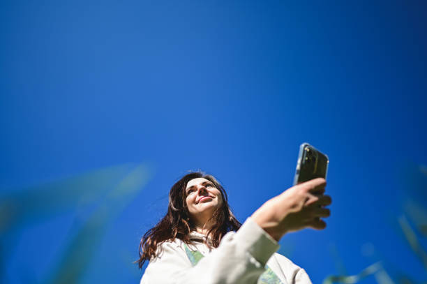 istock Young woman taking pictures with smartphone under blue sky 2205896242