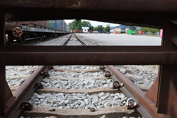 Perak, Malaysia - July 6, 2024 : A detailed view of train tracks at an inland port, featuring shipping containers and industrial buildings in the background. Ideal for illustrating logistics, transportation, and industrial themes.
