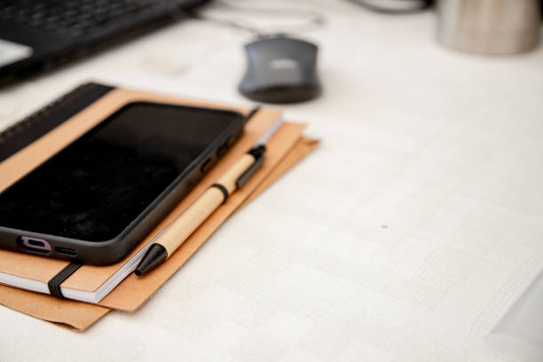 istock A neatly arranged workspace with a smartphone, notebook, and pen on a desk, ready for work or study. The blurred background with a laptop and mouse suggests a productive or creative session. 2205900548