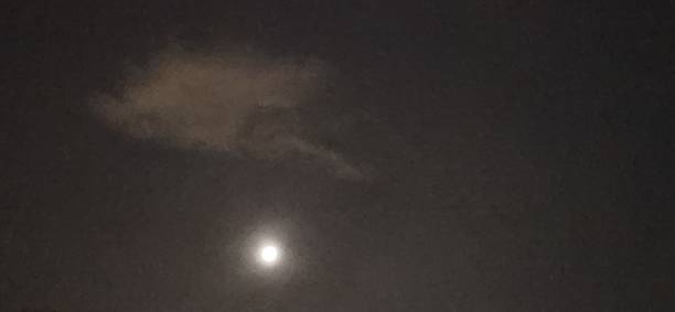 The full Moon shines through the gaps in the clouds, its soft glow creating a diffused effect in the darkness. The interplay of light and shadow makes the night sky even more enigmatic and fascinating.