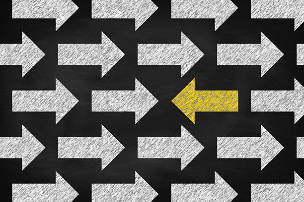 istock Yellow arrow goes in a different direction from the white arrows. Be different, standing out from the crowd . Chalk on the blackboard. 2205912667