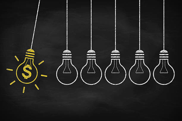 istock Newton's cradle concept. Hanging light bulbs with dollar sign on black chalkboard. 2205915180