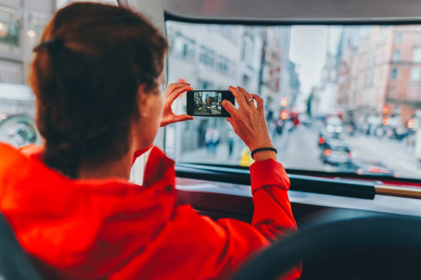 Smiling african millennial woman taking a selfie in London with a red double-decker bus and Big Ben in the background. Travel portrait that conveys joy, sightseeing and city energy.
