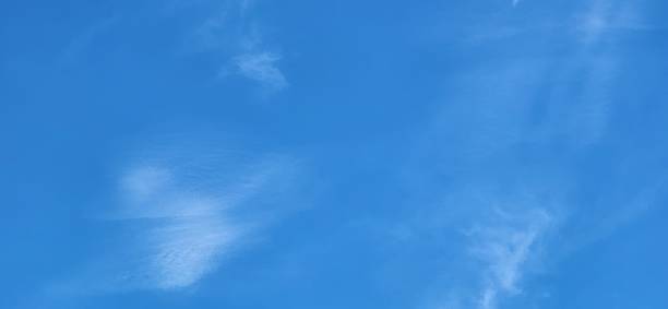 The blue sky is framed by scattered cirrus clouds, gliding gently with the high-altitude winds. Their thin and elegant appearance adds lightness and fluidity to the celestial landscape.