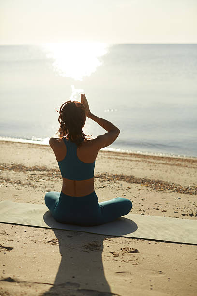 istock Woman Practicing Yoga On Beach At Sunrise, Facing The Ocean 2205919817