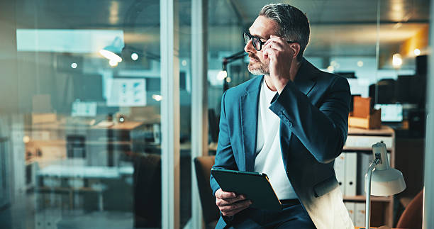 istock Night, thinking and man on tablet for office report, post deadline or online update research. Mature person, engagement or content strategy for digital marketing trends or social media growth on tech 2205924346