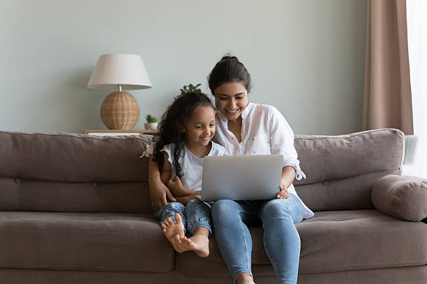 istock Indian woman and daughter sit on sofa with laptop 2205924698