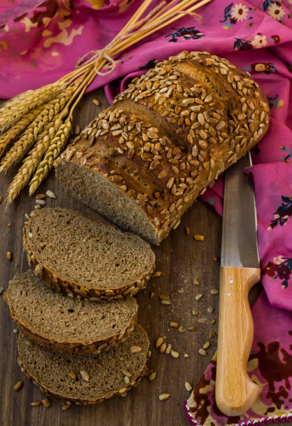 Close-up taken of sliced of cereal bread on wooden table with a bunch of wheat ears,top view
