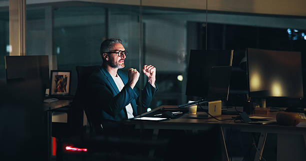istock Business, man and celebration with laptop at night for software development or troubleshooting success. Web developer, mature person and victory fist for website maintenance or system update deadline 2205925515