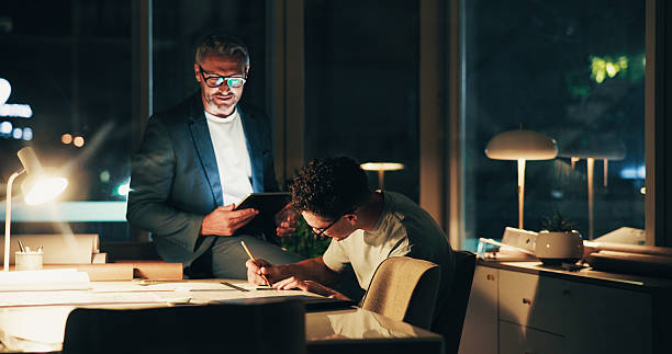 istock Architecture, night and men in office for urban planning advice, property design and floorplan. Creative agency, working late and architect with layout, blueprint and ideas for building project 2205925541