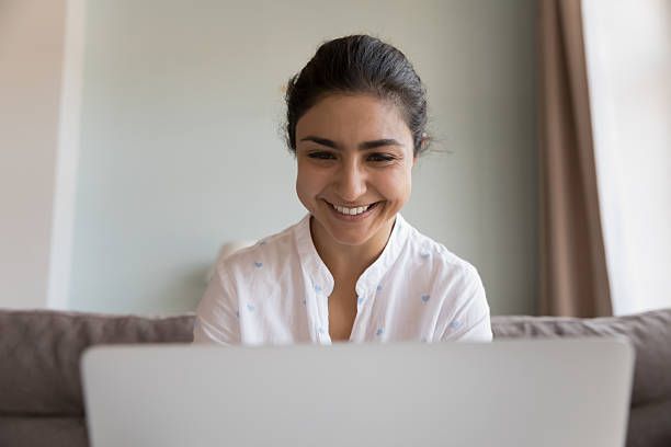 istock Happy Indian woman using laptop seated on sofa at home 2205927493