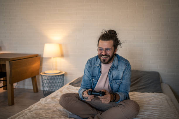 istock Young man sitting on bed playing video games and having fun 2205928977