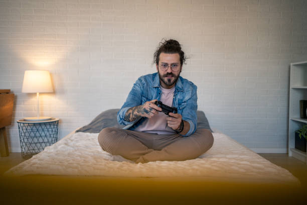 istock Young man playing videogames sitting on bed in modern apartment 2205928986