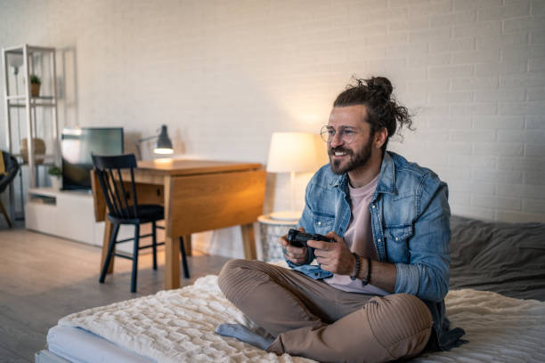 istock Young man relaxing on bed playing video games in modern apartment 2205928994