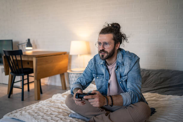 istock Young man playing videogames sitting on bed in modern apartment 2205929002