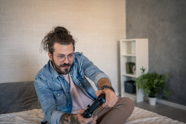 istock Young man playing videogames on the bed at home 2205929021