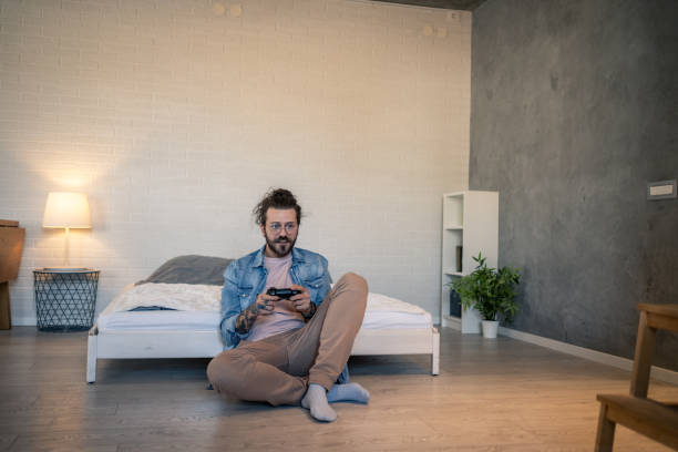 istock Young man playing videogames sitting on bedroom floor 2205929076