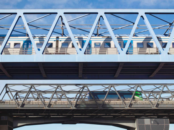 Two truss bridges, a railway bridge in front with a train crossing and a highway bridge with a truck in the background.
