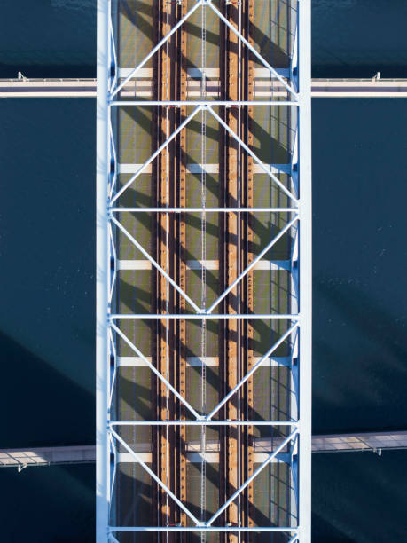 A truss bridge for railway traffic viewed from above, the sunlight casting a pattern from the bridge beams on the tracks.