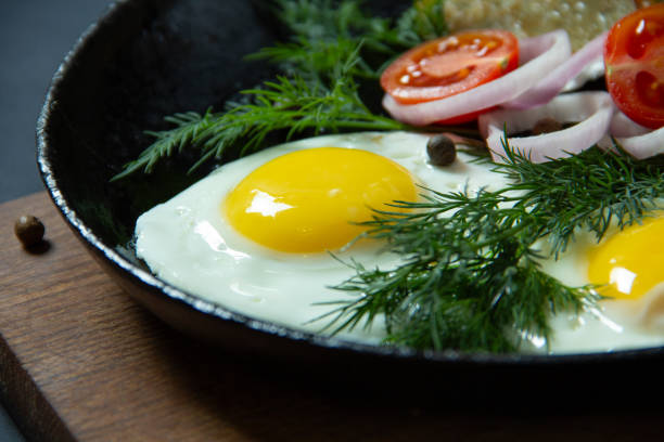 hot fried eggs with potato pancakes on a cast iron frying pan together with greens and vegetables on a black background