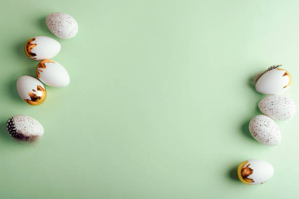 istock White and gold Easter eggs with speckled patterns and feathers arranged on a pastel green background. Top view, flat lay, copy space 2205934474