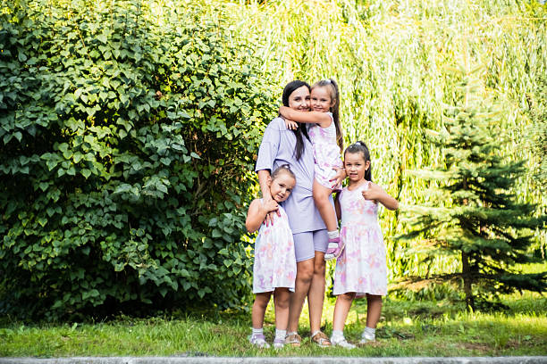 The three sisters stand close together, hugging their mother tightly. The younger twins, smile brightly as they lean into her embrace. Their older sister holds on lovingly.