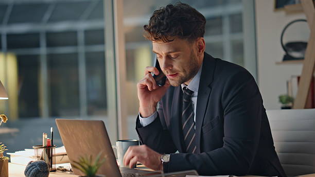 istock Late worker talking cellphone at office desk with serious expression closeup. 2205937900