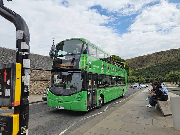 Edinburgh, Scotland, UK - August 3, 2024: Double decker city tour bus, Edinburgh. Edinburgh during the Edinburgh Fringe Festival. There are people relaxing. At the background Arthur's Seat and on the left building exterior of The Cafe at the Palace