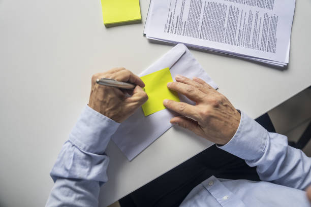 istock Elevated view of unidentified person's hands writing on yellow adhesive note 2205939800