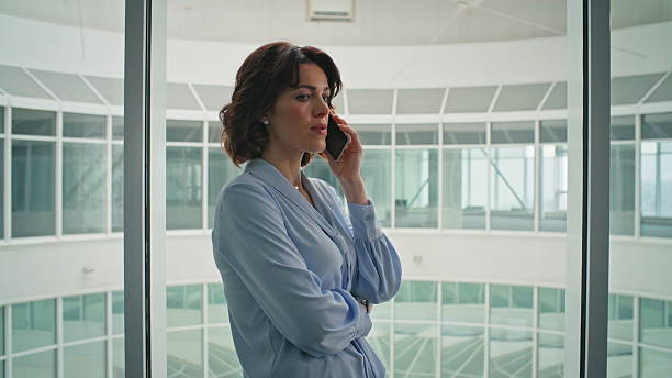 istock Lady boss communicating cellphone standing by office window closeup zoom out. 2205940293