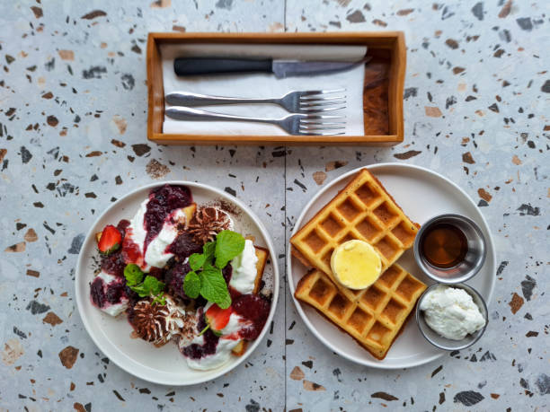 Berry Paradise Waffle With Strawberry Compote, Strawberry Fruit, Cheese Cream, Biscuit, Chocolate Powder And Fresh Mint Leaves. The Classic Waffle With Butter, Cheese Cream And Maple Syrup. Dessert Food Menu. Top View.