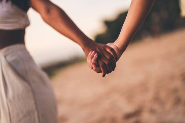 istock Close-up of two people holding hands on a sandy beach during sunset 2205945186
