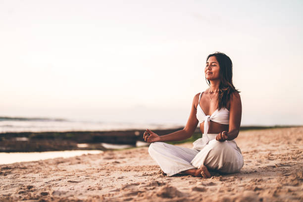 istock Young woman meditating on the beach during sunset in a serene atmosphere 2205945193