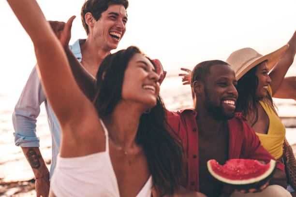 Group of friends enjoying drinks and watermelon slices during a sunny beach day A joyful group of friends enjoys a sunny day at the beach, holding watermelon slices and sharing laughs. The image radiates happiness, friendship, and the carefree spirit of summer gatherings. black man eating watermelon stock pictures, royalty-free photos & images