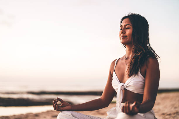 Woman practicing mindfulness meditation on a serene beach during sunset in summer