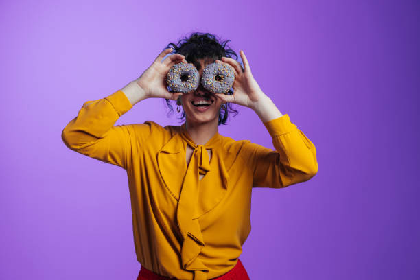 istock Playful young woman covering her eyes with two donuts 2205945547