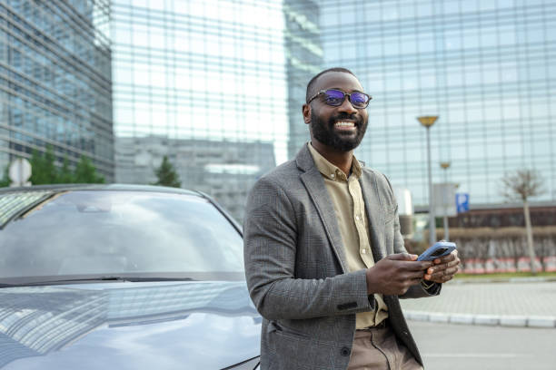 istock Businessman leaning on car while using phone outside modern office building 2205946288