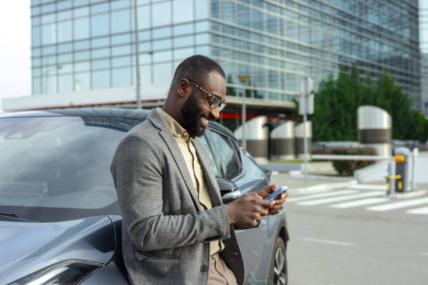 istock Man leaning on car with smartphone near modern office building 2205946319