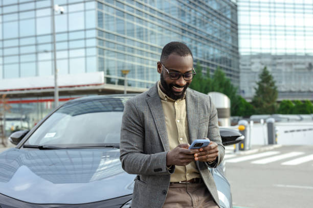 istock Man leaning on car with smartphone near modern office building 2205946329