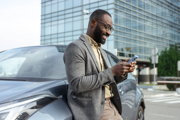 istock Businessman leaning on car while using phone outside modern office building 2205946341