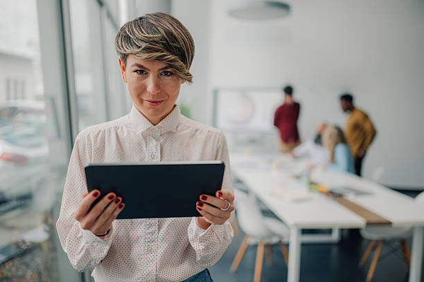 istock Young businesswoman using digital tablet in modern office with colleagues working in background 2205951912