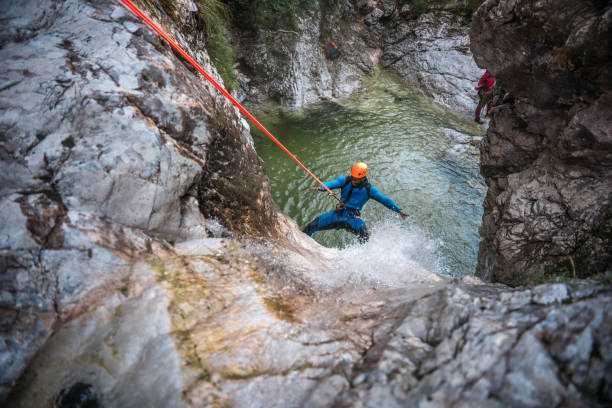 a black male, suited up in neoprene and helmet, conquers the canyons with bold descents while canyoning.