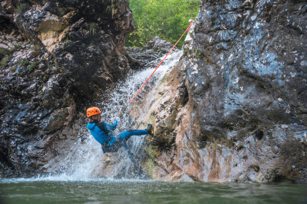 The excitement of canyoning, a black male, confidently navigating rocky terrain in a neoprene suit and helmet.