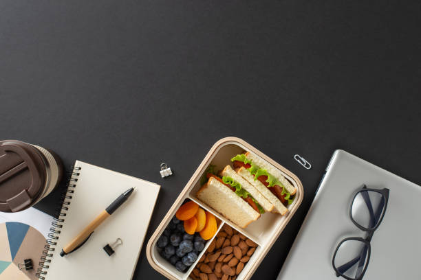istock Lunchbox with healthy food, a coffee cup, and accessories on a dark table setting 2205956960