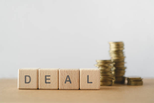 istock DEAL text on wooden cabe blocks with blurred stack of coins including copy space 2205958826