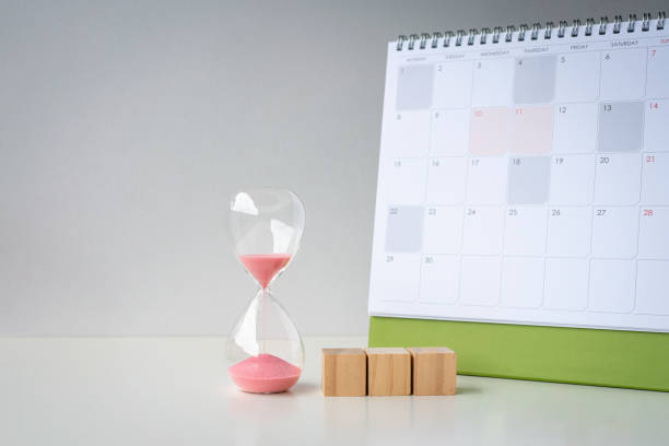 istock Sand timer with three blank wooden toy blocks next to a calendar. 2205962626